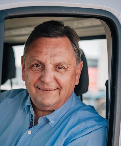 Christoph Boeckels sitzt hinter dem Steuer eines Kleintransporters und blickt, freundlich lächelnd, aus dem Seitenfenster des Kleintransporters heraus.
